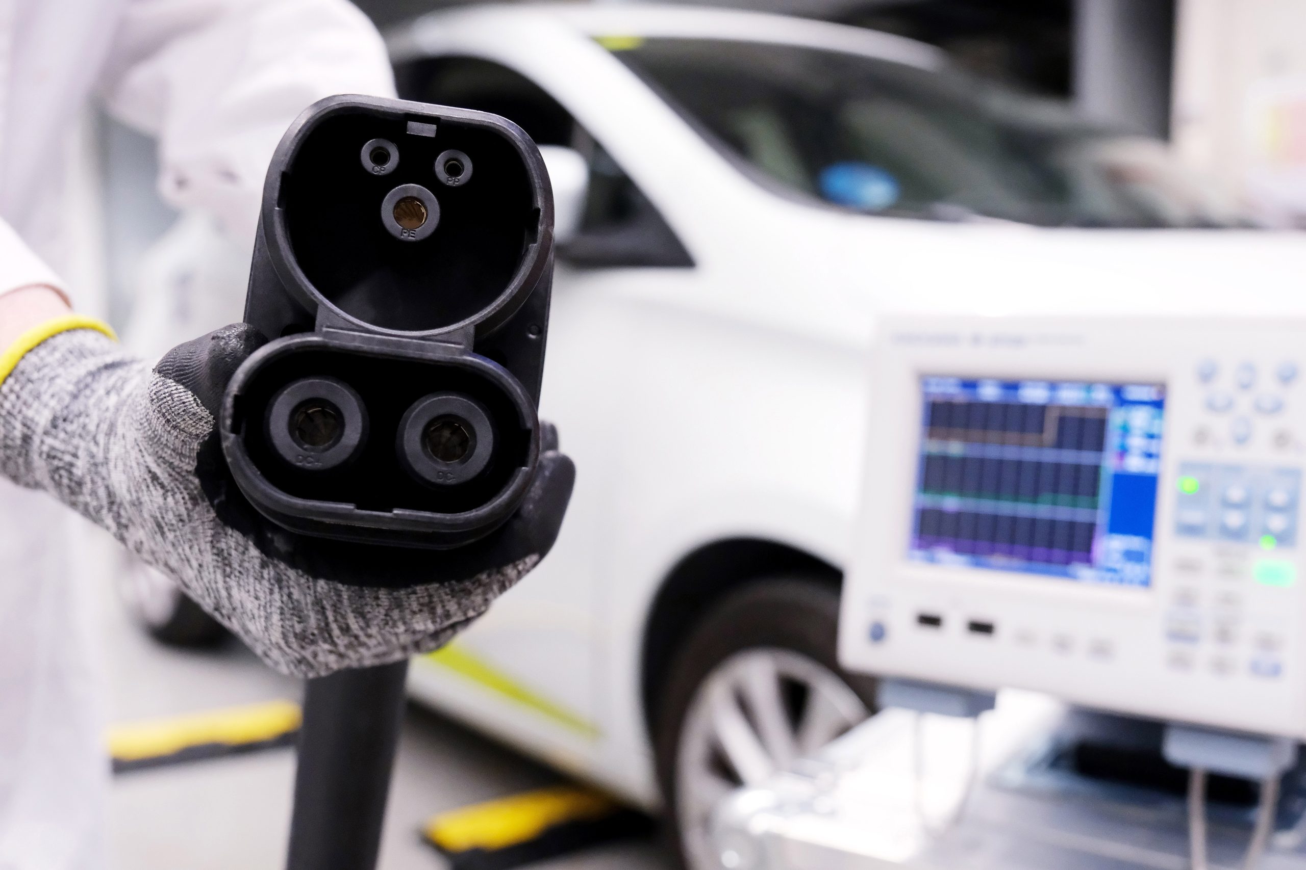 Technician interacting with a large-scale electric charging connector in a smart energy system environment, with an electric vehicle in the background, representing energy systems integration and smart grid technologies.