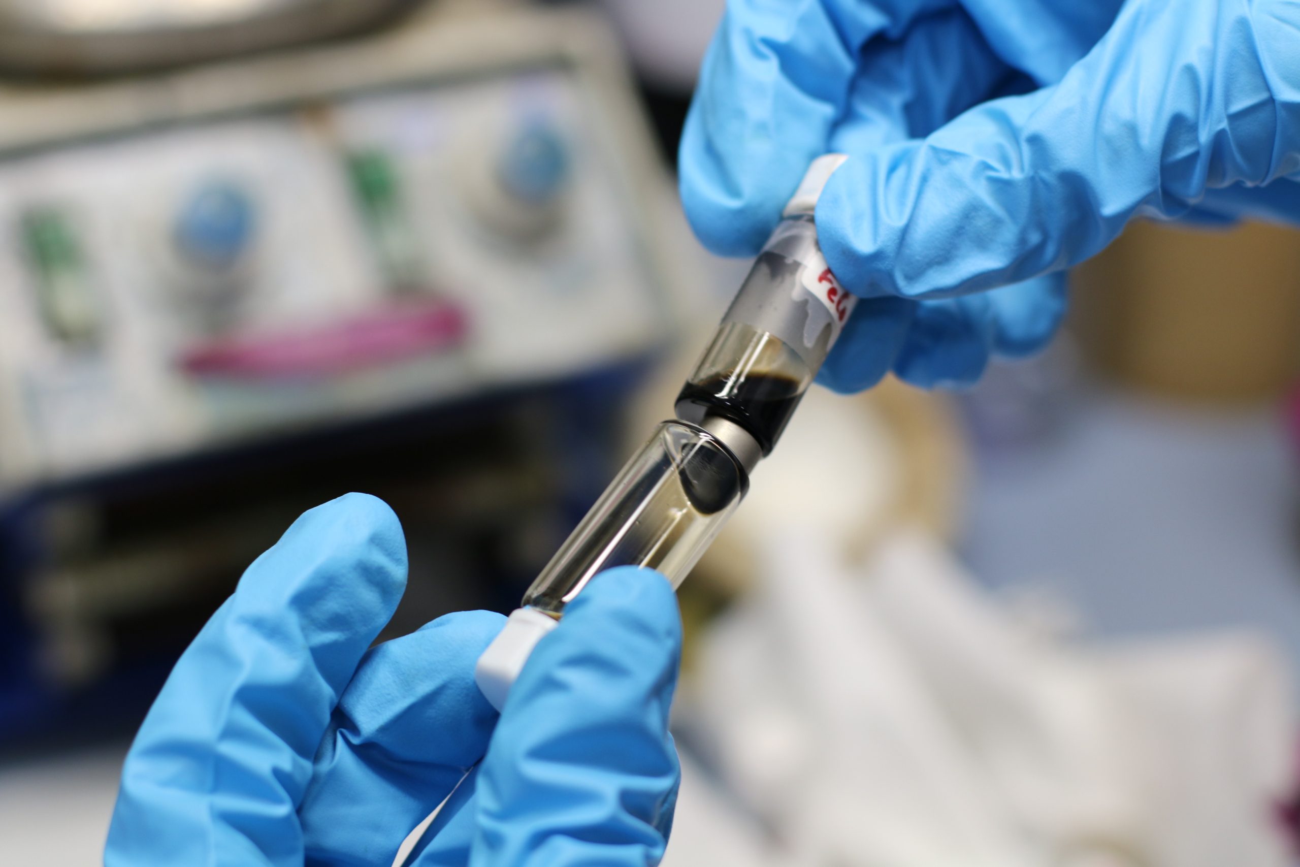 Scientist transferring liquid between laboratory containers, representing solution-based synthesis and flow-reactor processes for nanoparticle and nanocomposite fabrication with controlled composition and morphology.
