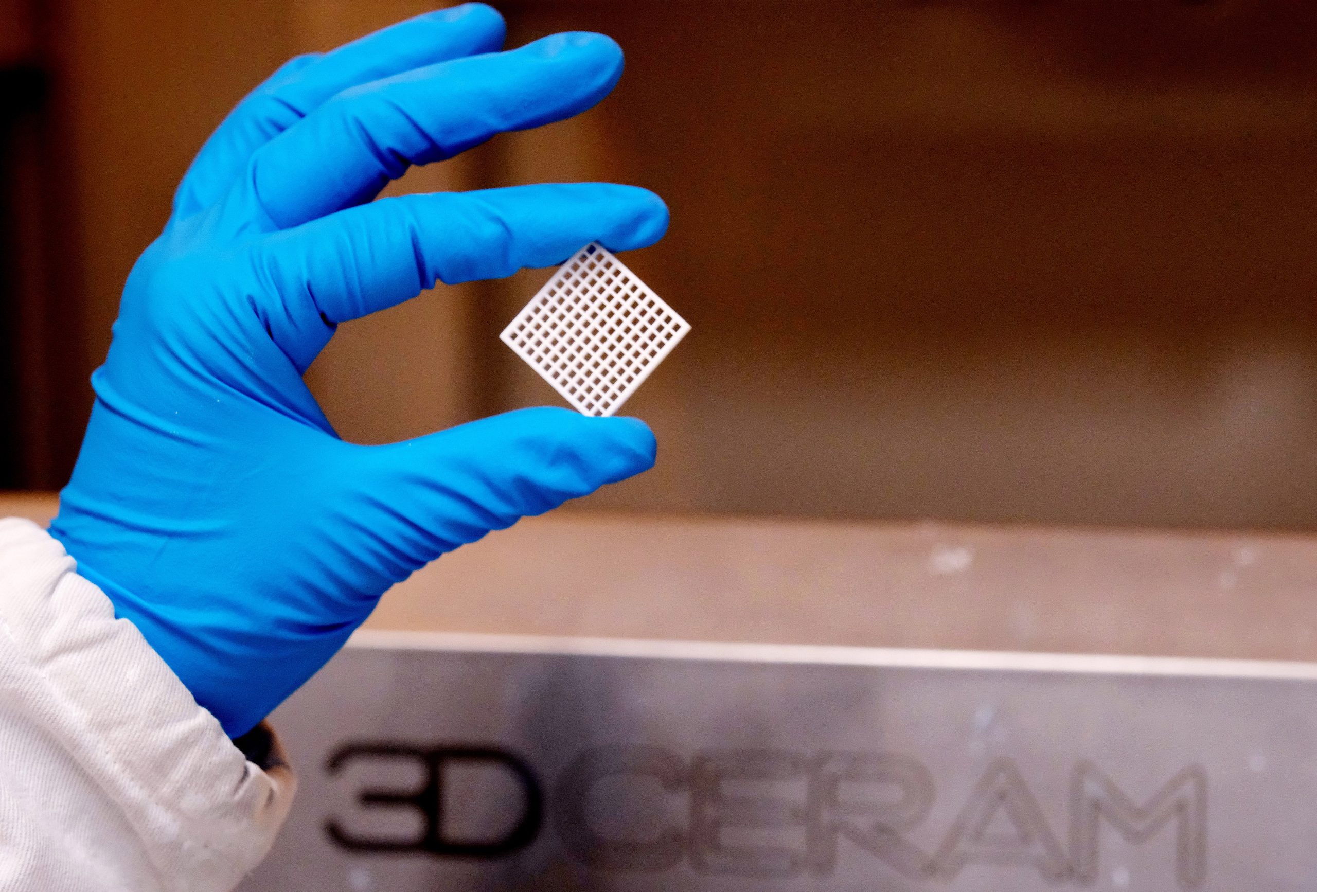 Scientist presenting a small grid-like ceramic component used in advanced 3D-printed energy devices for solid-state batteries and fuel cell applications.