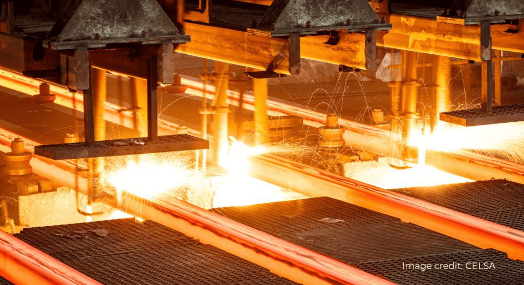 Glowing hot steel bars moving through an industrial rolling mill with bright sparks flying