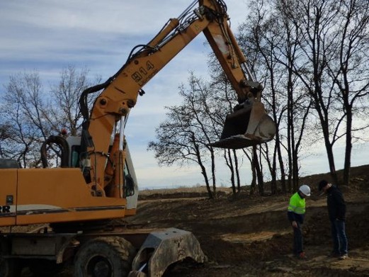 Excavator at construction site with two workers operating and supervising earthworks